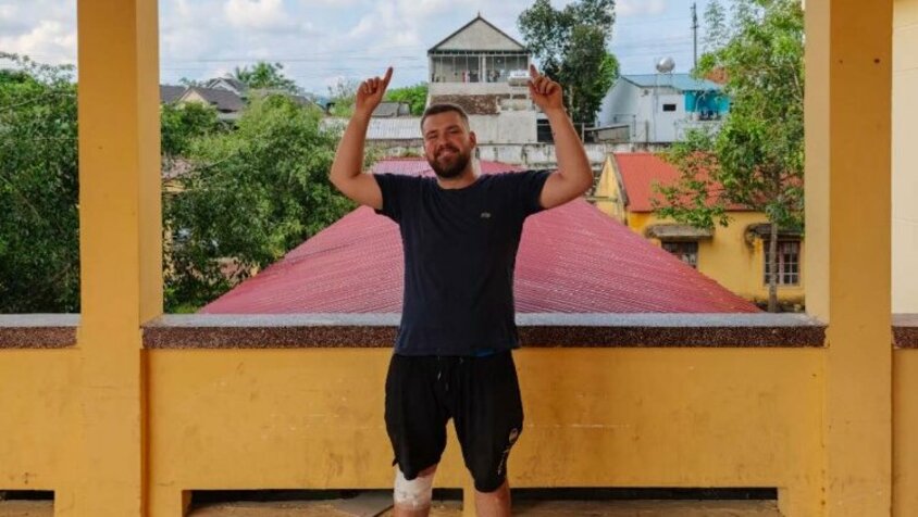 Jan Wengryn steht lachend unter einem Schild mit der Aufschrift „General Surgery Department“ in Vietnam, zeigt mit beiden Armen nach oben und nimmt die Situation mit Humor – eine Momentaufnahme seiner Reise durch Südostasien.