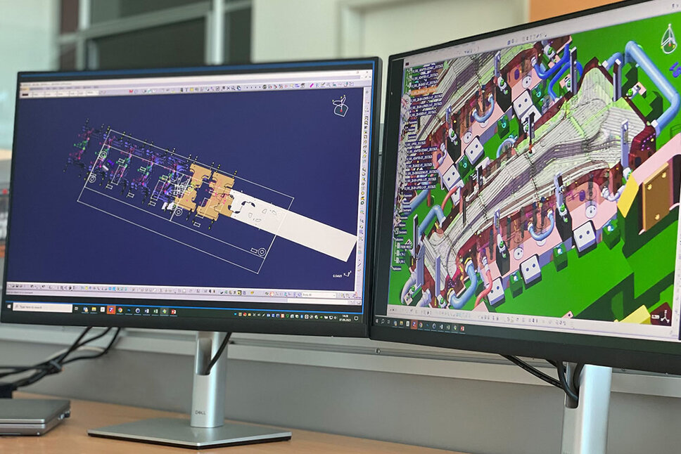 Dvě obrazovky počítače, jedna zobrazuje detailní detail CAD návrhu nástroje pro tváření za tepla pro výrobu B-sloupků, zatímco druhá obrazovka zobrazuje přenosovou strukturu nástroje.