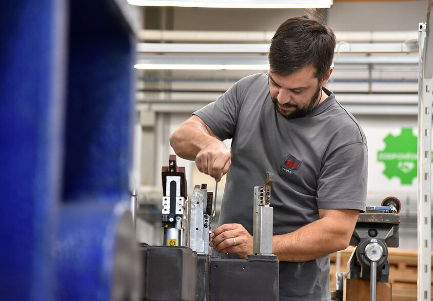 Ein Metalltechniker bei weba Werkzeugbau in Aktion, konzentriert auf den Zusammenbau von Messaufnahmen in der Produktionshalle. Der Techniker, in sauberer und praktischer Arbeitskleidung, arbeitet präzise an einem gut beleuchteten Arbeitstisch. Umgeben von verschiedenen Werkzeugen und Bauteilen, zeigt das Bild den Detailreichtum und die Präzision, die im Werkzeugbau erforderlich sind. Die Szene vermittelt ein Gefühl von Fachwissen und Engagement im Produktionsprozess, charakteristisch für die hohe Qualitätsstandards bei weba.