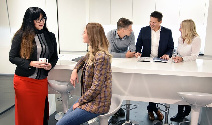  Employees of weba Werkzeugbau are standing in the coffee kitchen, engaging in conversation.