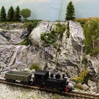 Schwarze Modell-Dampflokomotive mit Güterwagen vor einer detailreich gestalteten Felslandschaft.