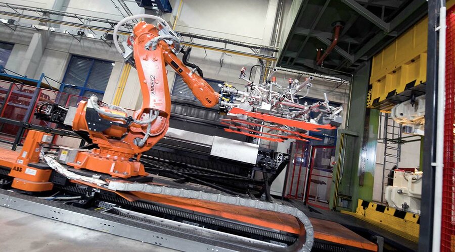 Robotická ramena přenášejí čtyři rozžhavené polotovary z komorové pece do formy pro lisovací kalení.