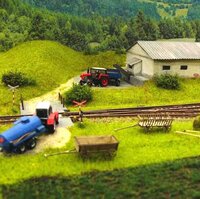 Detailreiche Modelleisenbahnlandschaft mit Gleisen, Bahnübergang, Traktoren, Anhängern und einem landwirtschaftlichen Gebäude.