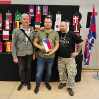 František Krumpolec steht gemeinsam mit zwei weiteren Modellbauern vor einer Ausstellung mit internationalen Flaggen.