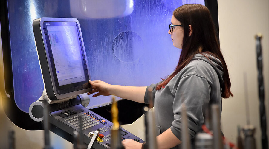 Na snímku je technik výroby nástrojů, který soustředěně pracuje na ovládacím panelu nejmodernějšího pětiosého obráběcího centra. Pomocí klávesnice a obrazovky sleduje a řídí proces obrábění. Scéna vyzařuje profesionalitu a technické znalosti, zatímco stroj v pozadí provádí vysoce přesné obráběcí úkony.