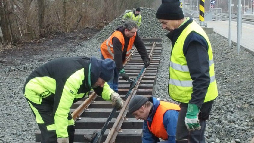 Mehrere Mitglieder eines Modelleisenbahnvereins arbeiten gemeinsam an Gleisen im Außenbereich.